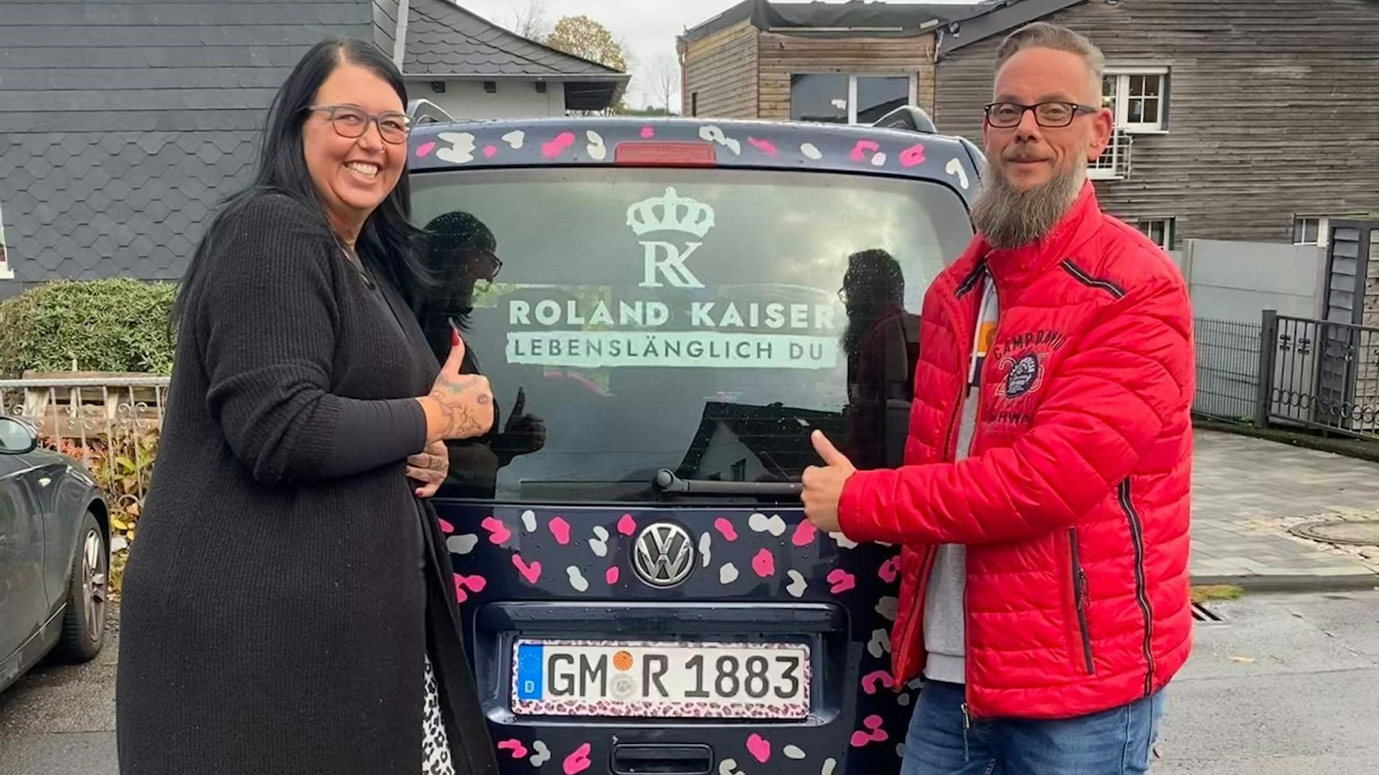 Blick auf ein Ehepaar, das hinter einem bunten Auto steht.