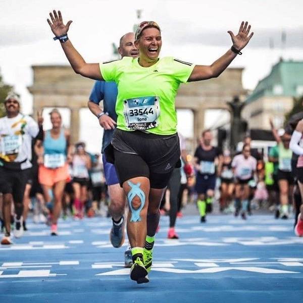 Die Läuferin Ilona Schaffrath (grünes T-Shirt) läuft beim Berlin Marathon jubelnd über die Ziellinie. Im Hintergrund ist das Brandenburger Tor zu erkennen.