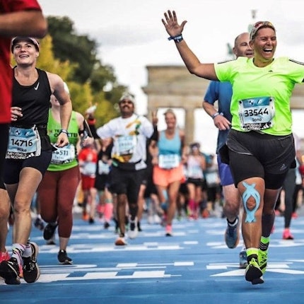 Die Läuferin Ilona Schaffrath (grünes T-Shirt) läuft beim Berlin Marathon jubelnd über die Ziellinie. Im Hintergrund ist das Brandenburger Tor zu erkennen.