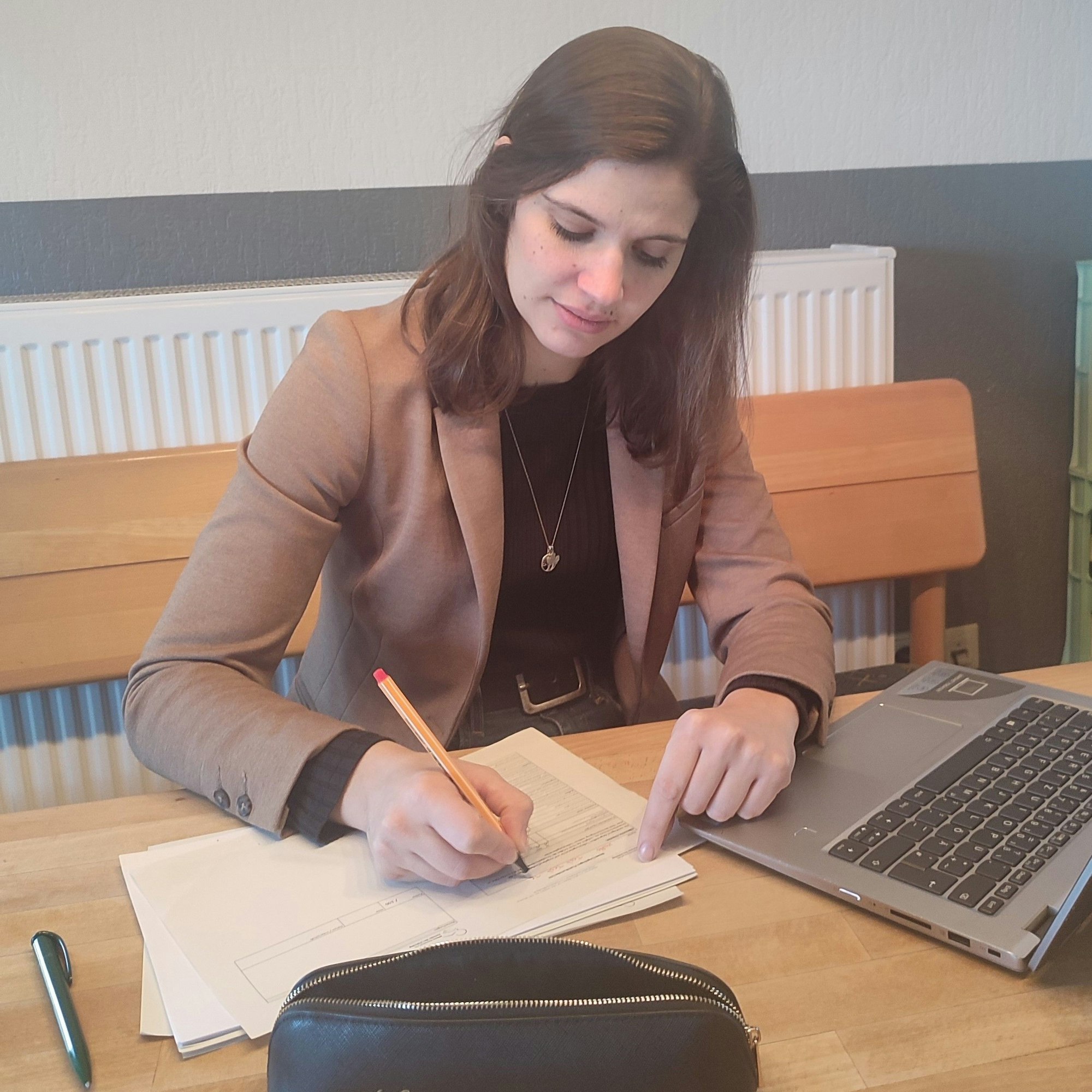 Kathrin Dahmen sitzt an einem Tisch und korrigiert mit einem Rotstift Aufsätze, vor ihr ein Laptop.