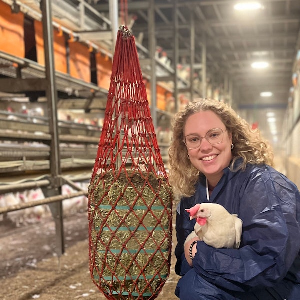 Jasmin Schleder im Stall, sie hält eine weiße Henne im Arm und lächelt in die Kamera.
