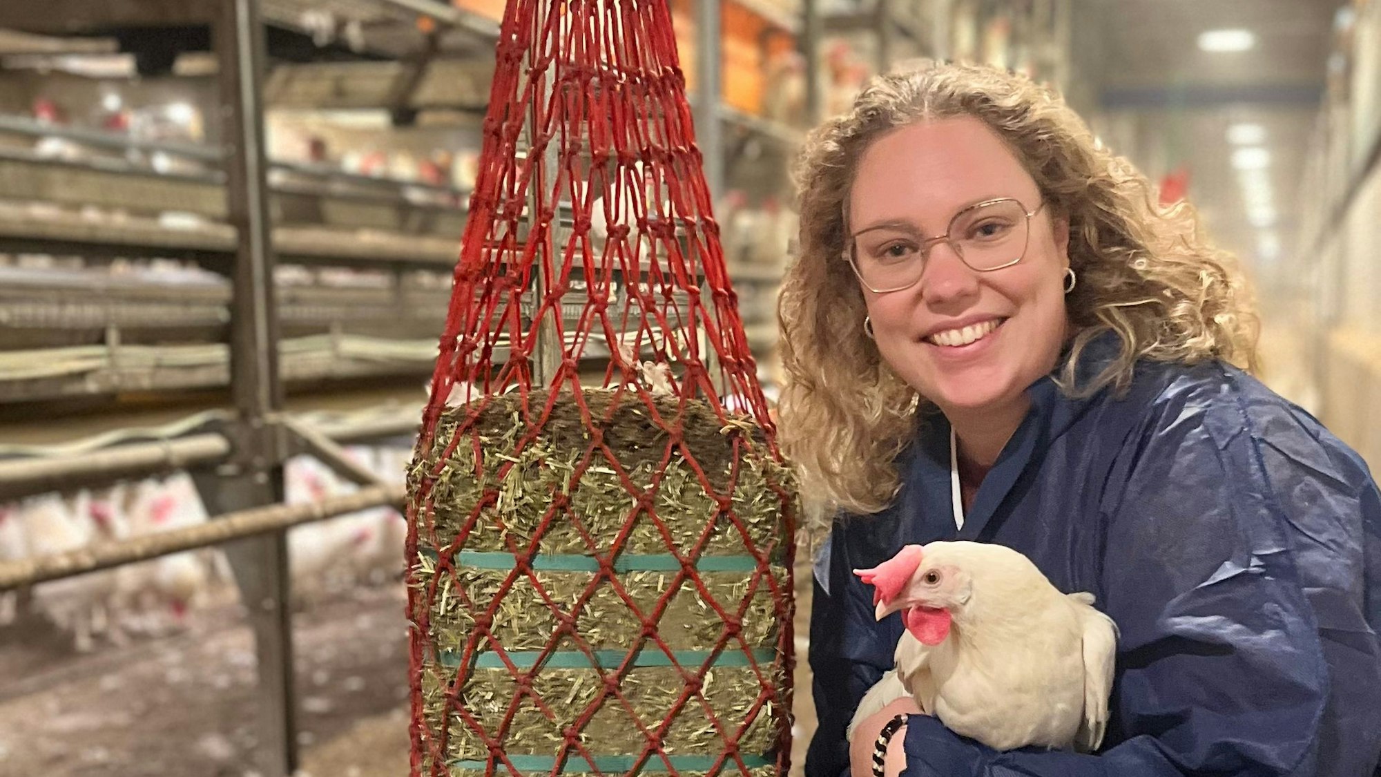 Jasmin Schleder im Stall, sie hält eine weiße Henne im Arm und lächelt in die Kamera.