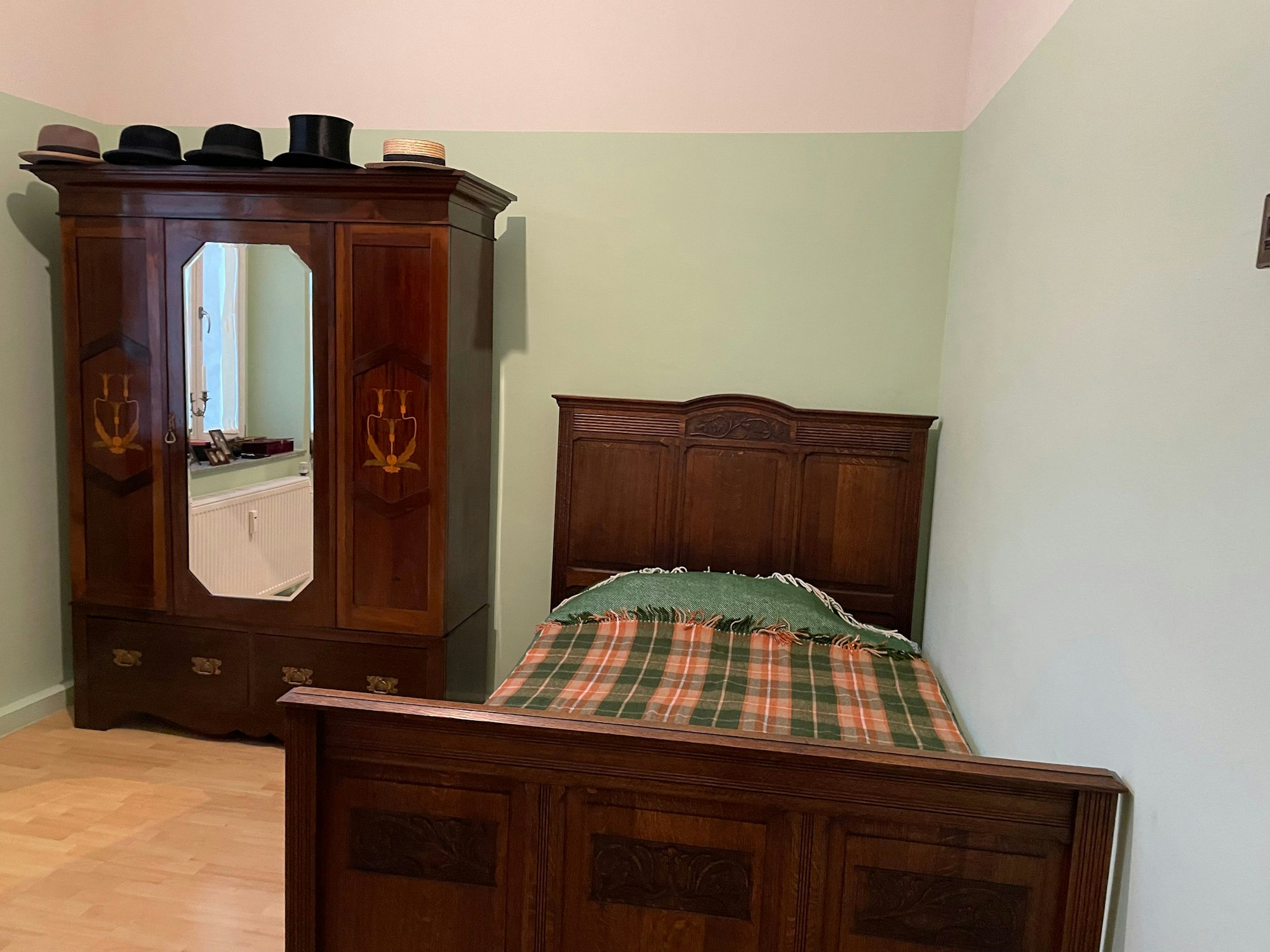 Ein antiker Holzschrank mit Spiegel steht neben einem wuchtigen Holzbett.