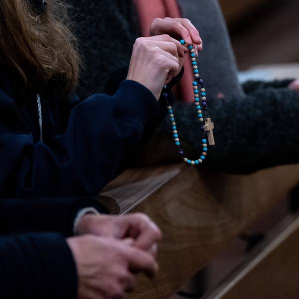 Eine Frau hält in der Kirche einen Rosenkranz in den Händen