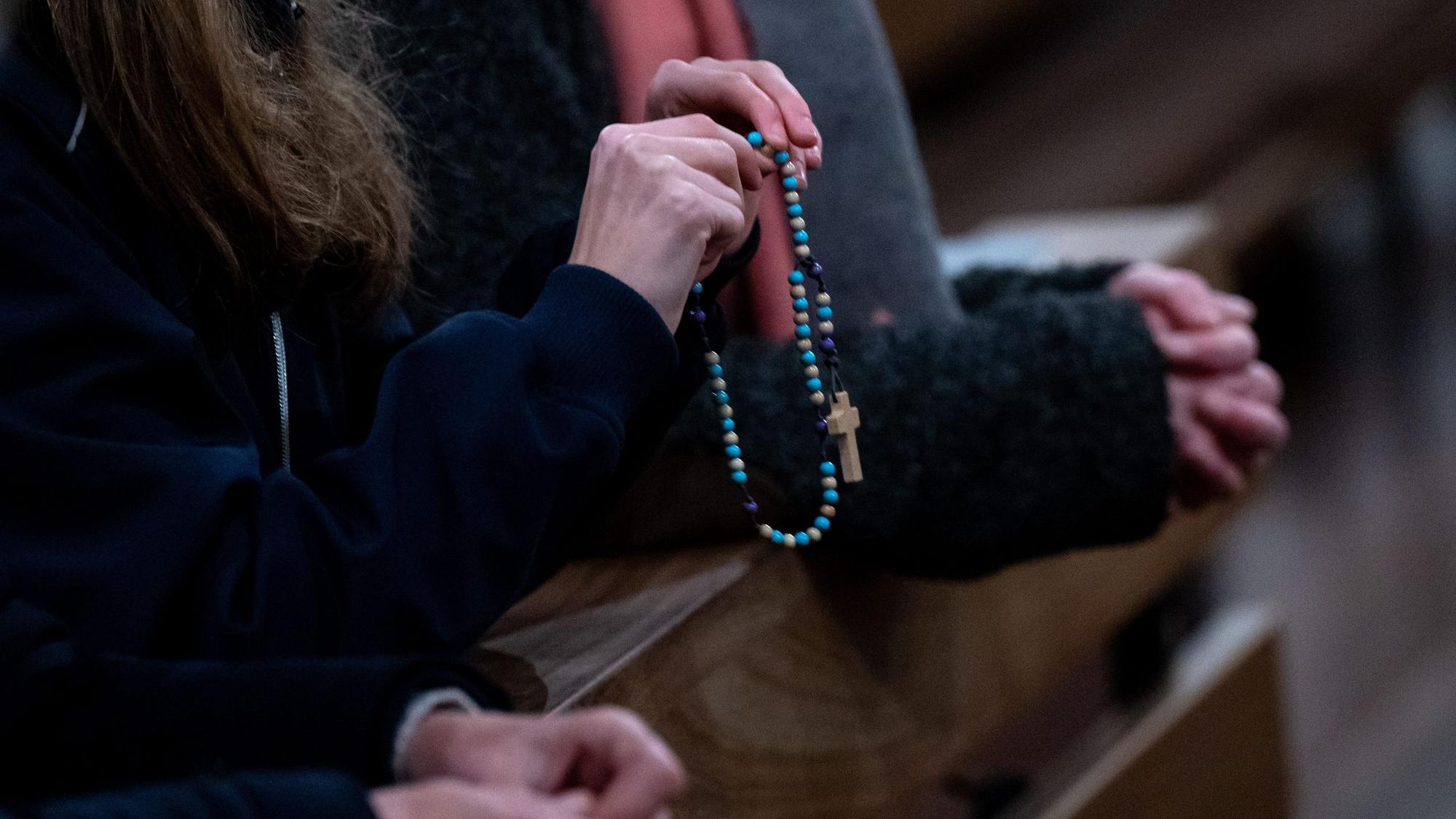Eine Frau hält in der Kirche einen Rosenkranz in den Händen