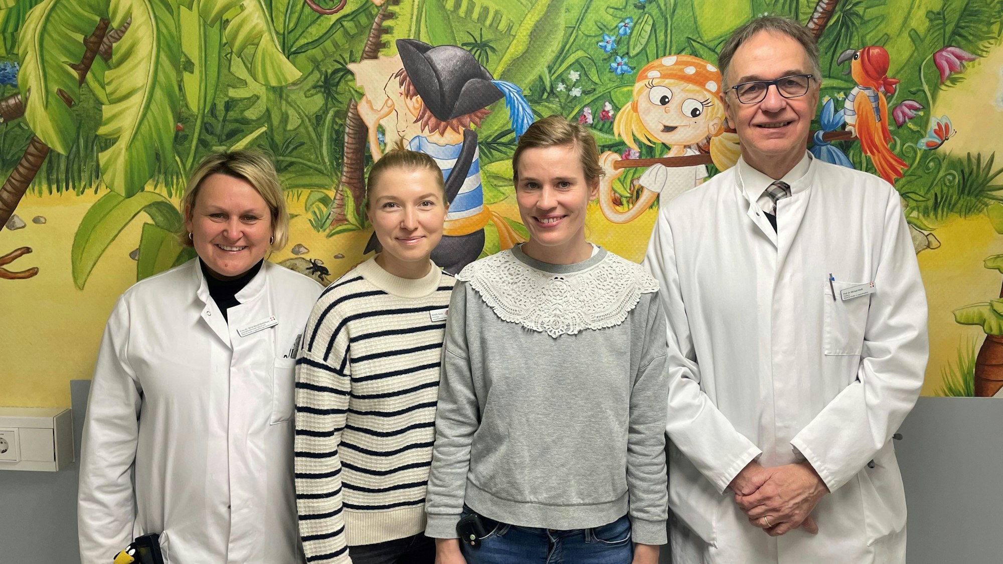 Das Team der Kinderschutzambulanz steht vor einer bemalten Wand.