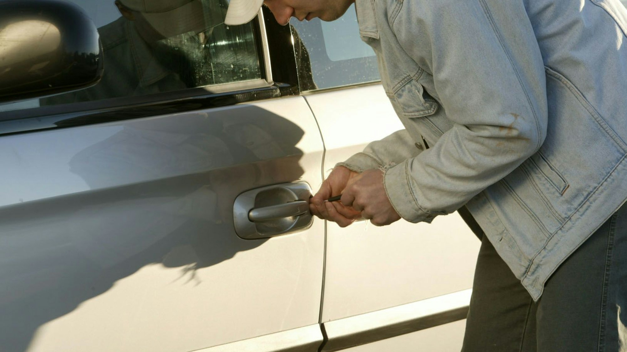 Das Bild zeigt einen Mann, der gerade versucht, ein Auto aufzubrechen.