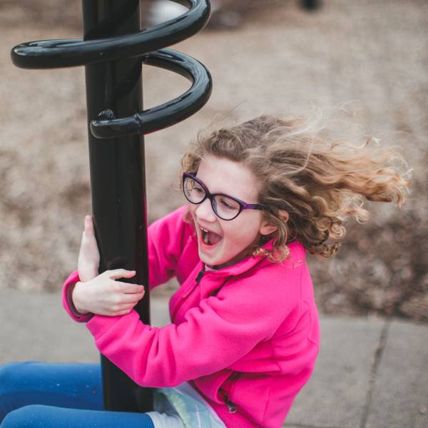 Ein knapp sechs- bis siebenjähriges Kind, das eine Brille trägt, spielt auf einem Spielplatz