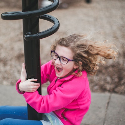 Ein knapp sechs- bis siebenjähriges Kind, das eine Brille trägt, spielt auf einem Spielplatz