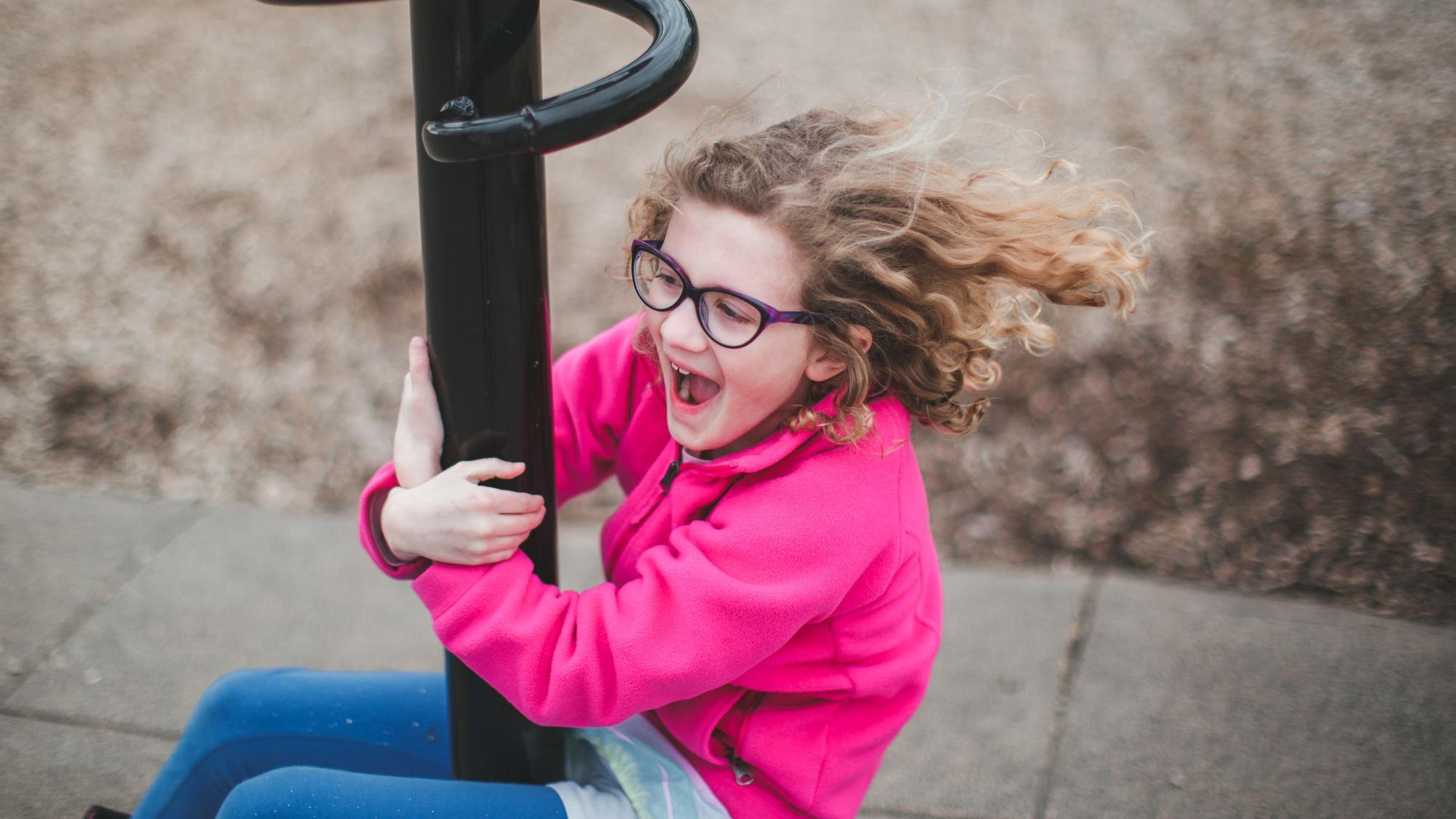 Ein knapp sechs- bis siebenjähriges Kind, das eine Brille trägt, spielt auf einem Spielplatz