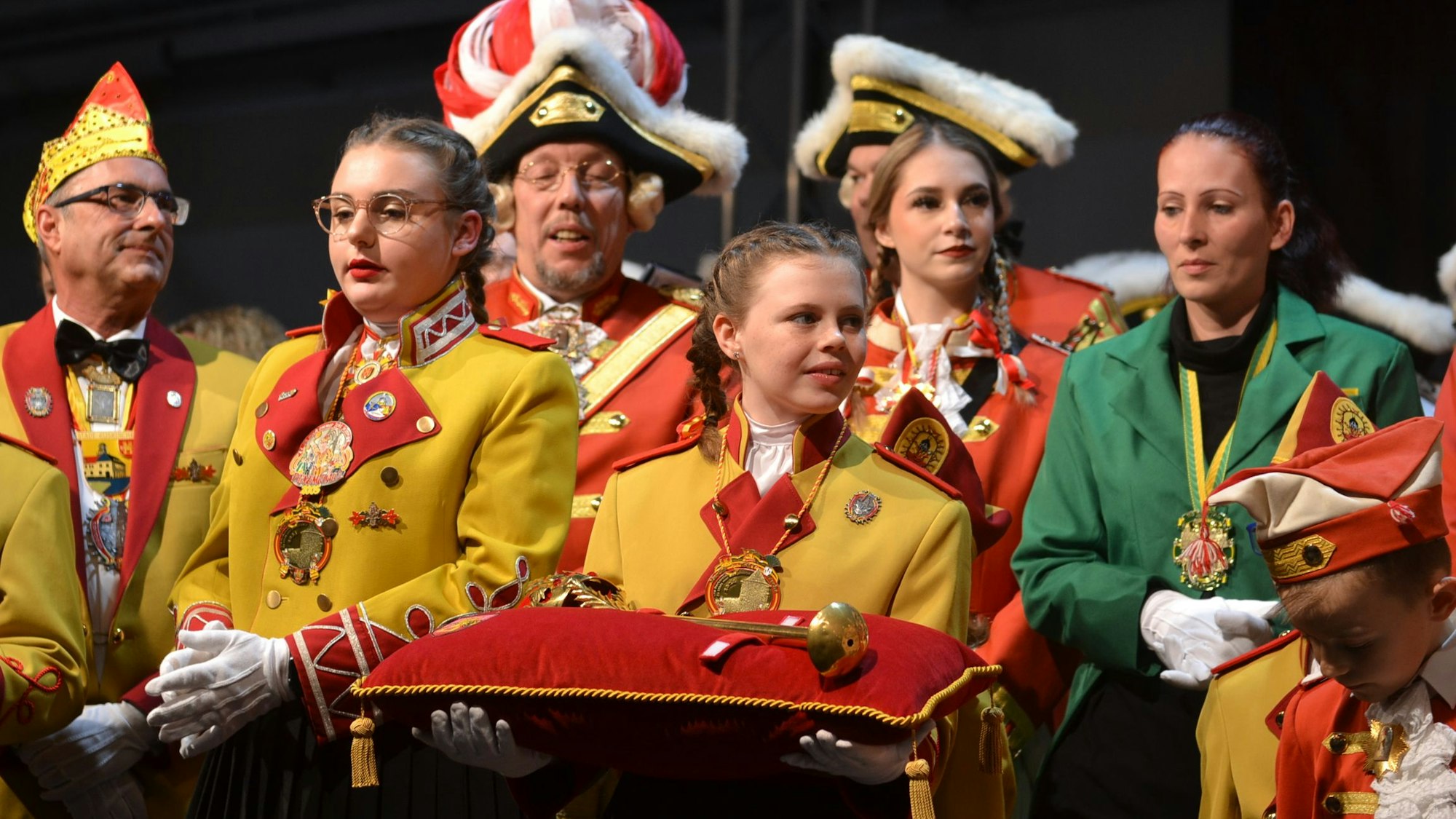 Junge Jecke in Uniform halten die Insignien auf einem Kissen.