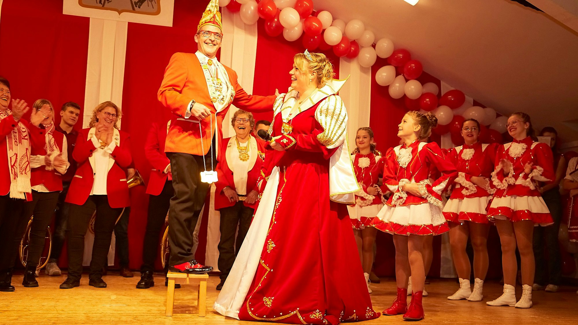 Prinzenführer Jürgen Hohn ist auf ein Fußbänkchen gestiegen und überragt die Prinzessin, seine Lebensgefährtin, nun um einen Kopf. In der Hand hält er den Orden. Im Hintergrund applaudieren Karnevalisten und junge Gardetänzerinnen.