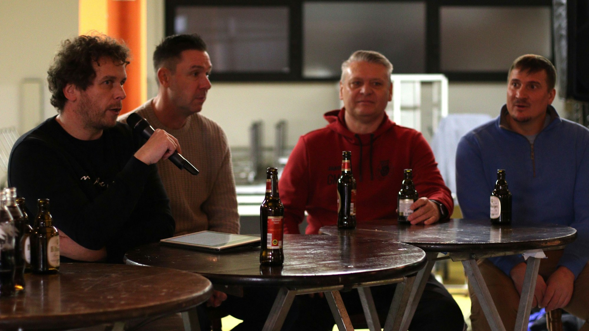 Moderator Tom Steinicke hält das Mikrofon in der Hand, neben ihm sitzen Uwe Metternich, Guido Mertens und Fabian Ewertz.