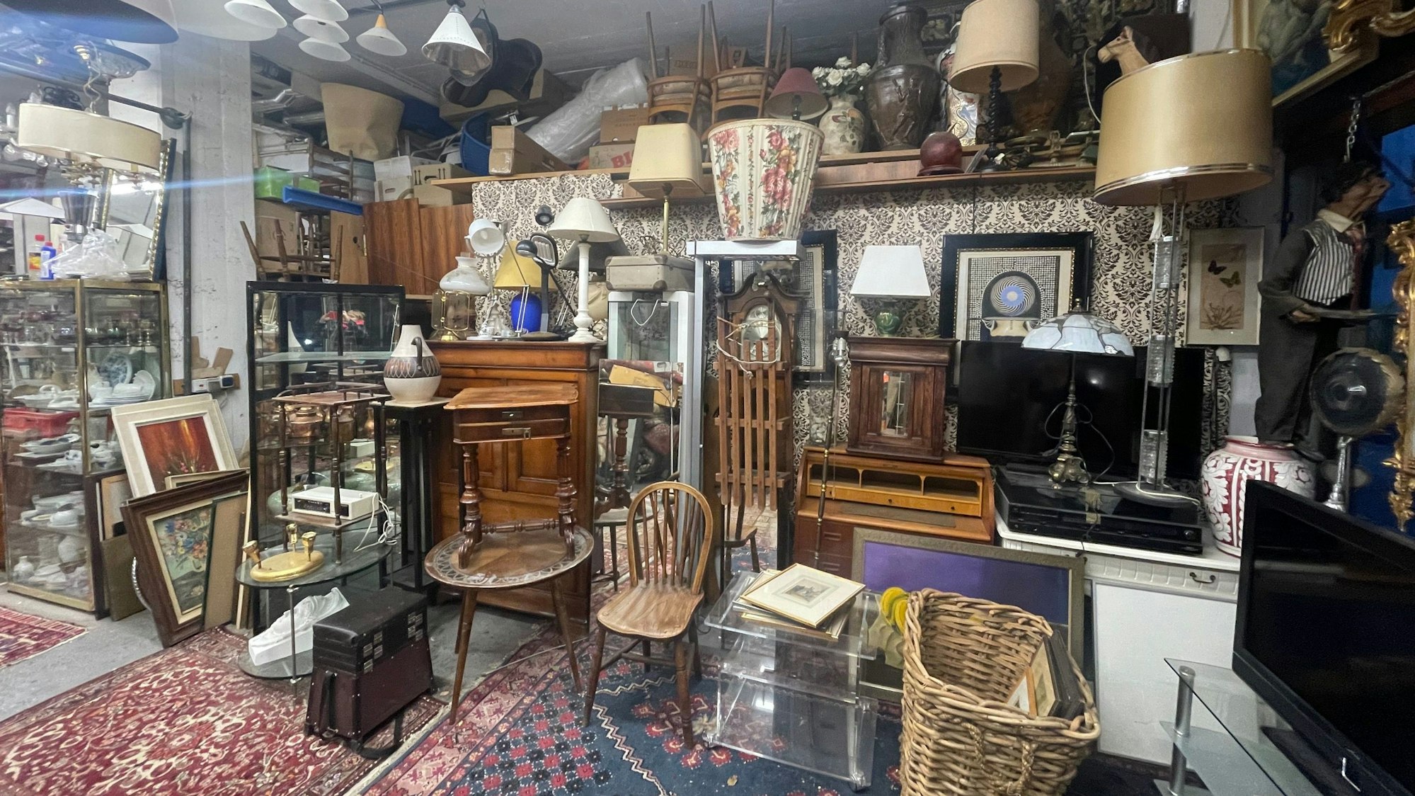 An einer Wand stehen viele Second-Hand-Möbel, an der Decke hängen alte Lampen.