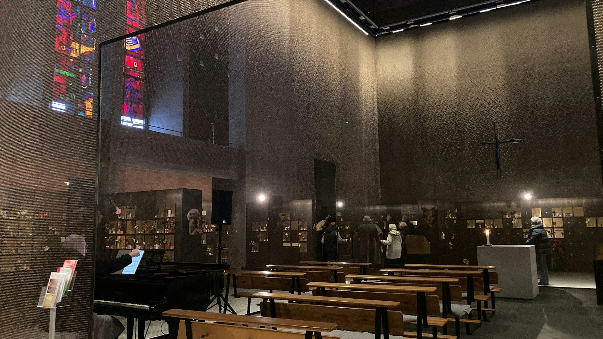 Der Innenraum einer Kirche mit Bänken, bunten Fenstern und einem filigranen netzartigen Vorhang aus Metall ist zu sehen.