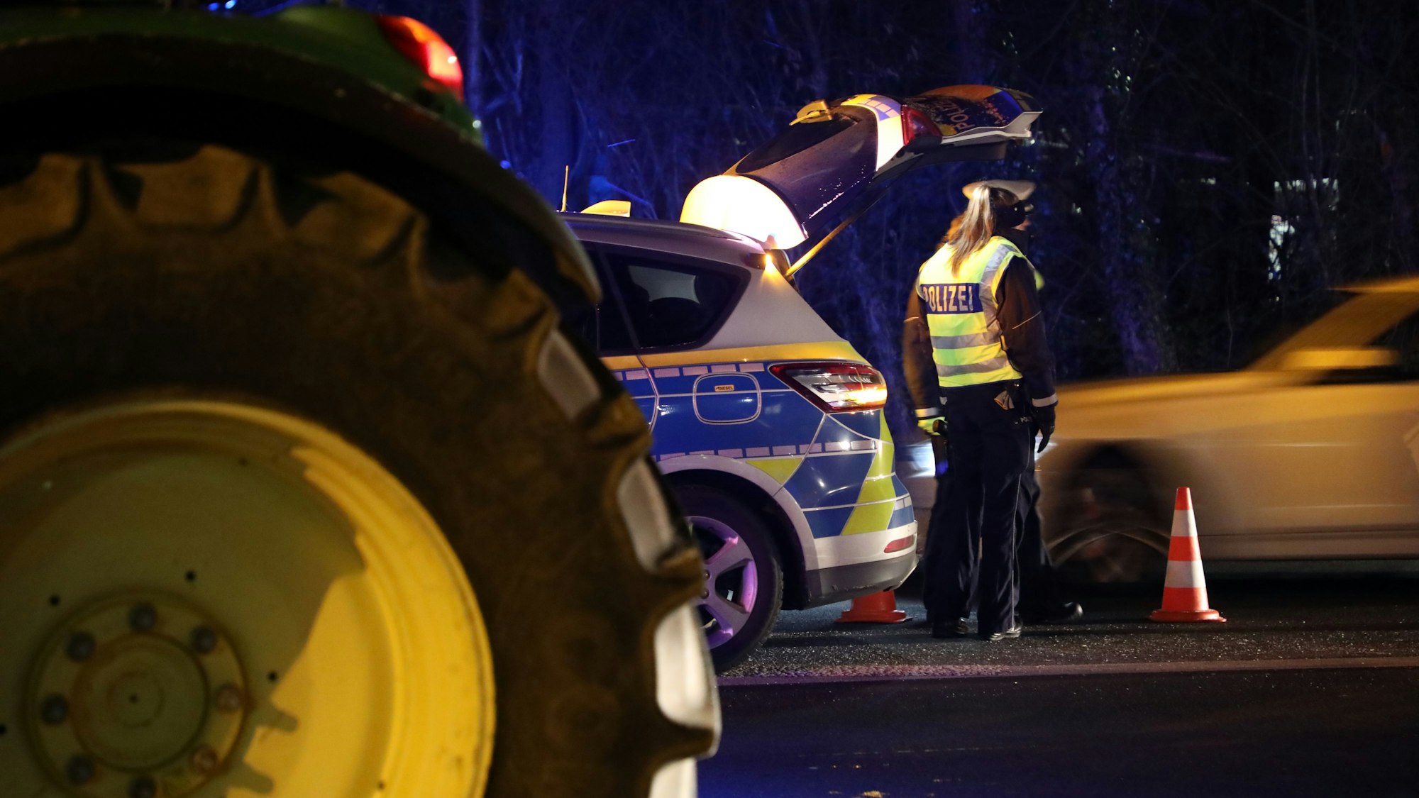 Polizistinnen stehen an einem Streifenwagen, im Vordergrund ist ein großer Traktorreifen zu sehen.