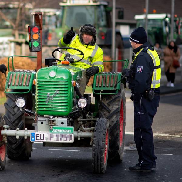 Das Bild zeigt einen Landwirt, der auf einem alten Traktor sitzt und mit einem Polizisten spricht.