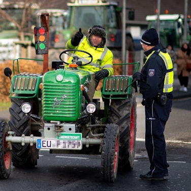 Das Bild zeigt einen Landwirt, der auf einem alten Traktor sitzt und mit einem Polizisten spricht.