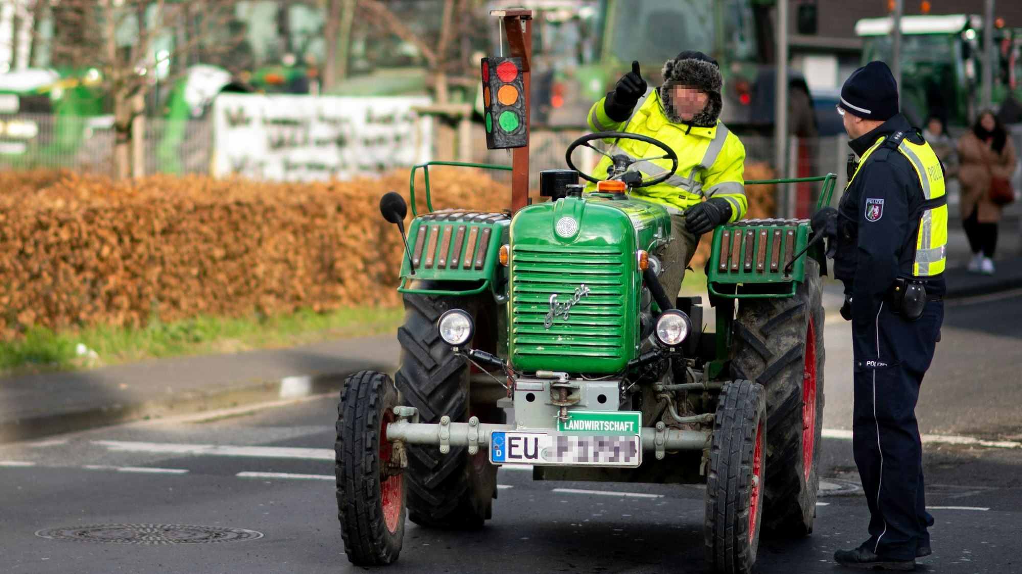 Das Bild zeigt einen Landwirt, der auf einem alten Traktor sitzt und mit einem Polizisten spricht.