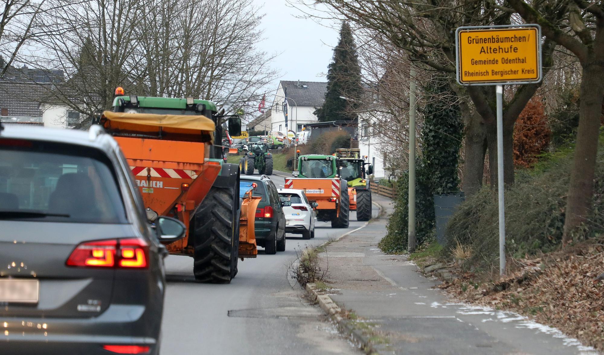 Am Ortsschild von Grünenbäumchen/Altehufe in der Gemeinde Odenthal ist eine Kolonne von Traktoren und Pkw zu sehen, die auf der B 506 in Richtung Bergisch Gladbach fahren.