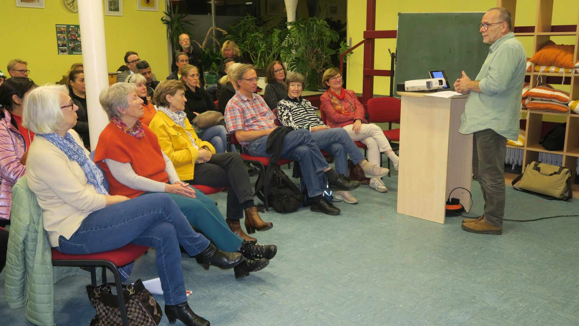 Zuhörer sitzen in einem Klassenraum und hören einem Vortragenden an einem Rednerpult zu.