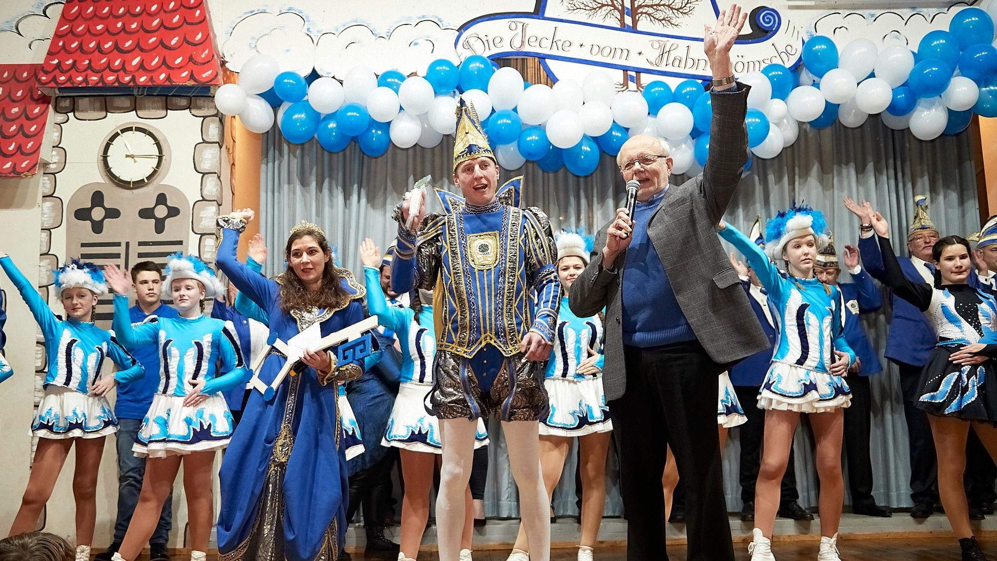 Das Prinzenpaar aus Scheven steht im Ornat auf der Bühne und lässt sich von Ortsvorsteher Hans Reiff feiern. Im Hintergrund steht eine Tanzgruppe, die Bühne ist mit blauen und weißen Luftballons geschmückt.