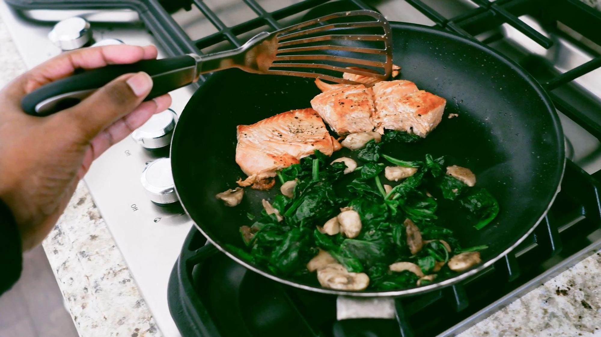 Eine Frau kocht Lachs mit Spinat in der Pfanne.