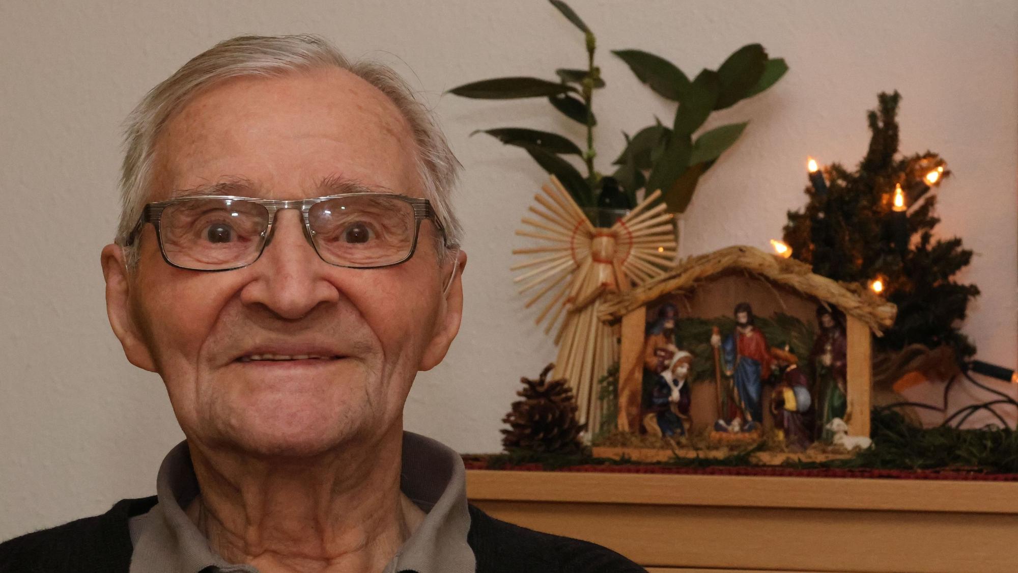 Ein alter Mann steht neben einer Weihnachtskrippe.