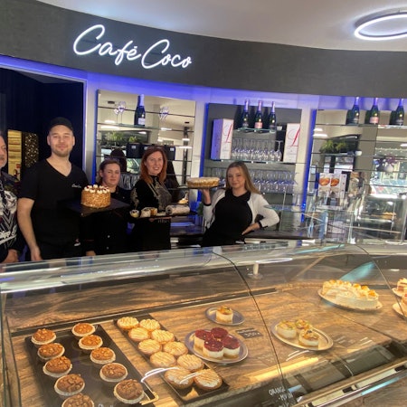 Drei Frauen und zwei Männer stehen hinter eine Kuchentheke