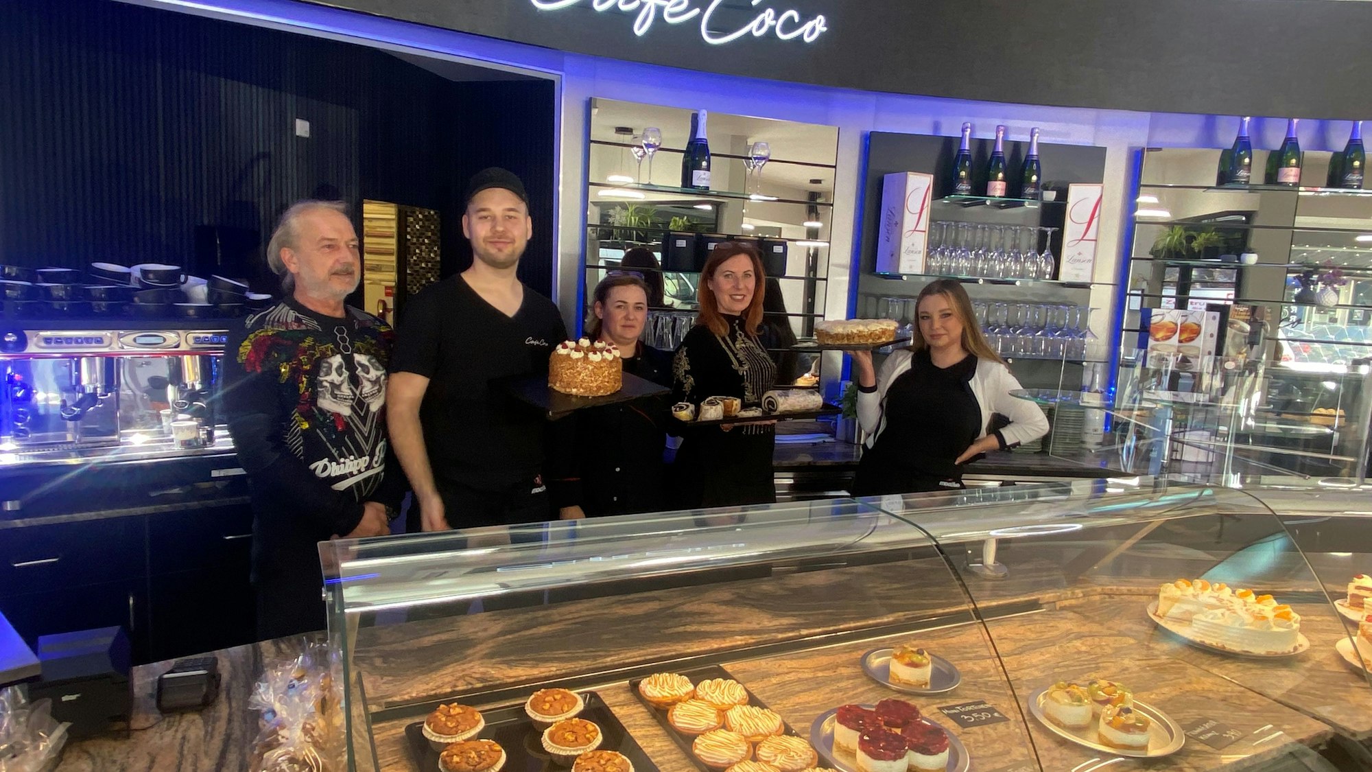 Drei Frauen und zwei Männer stehen hinter eine Kuchentheke