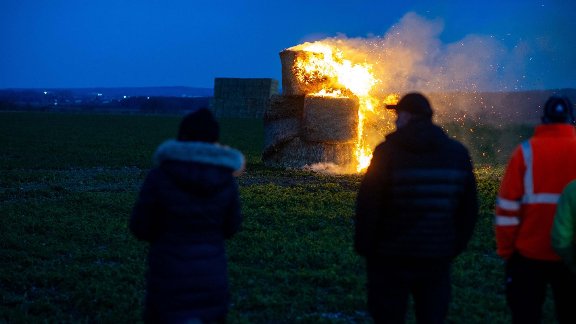 Ein Mahnfeuer aus Strohballen. Im Vordergrund mehrere Personen.
