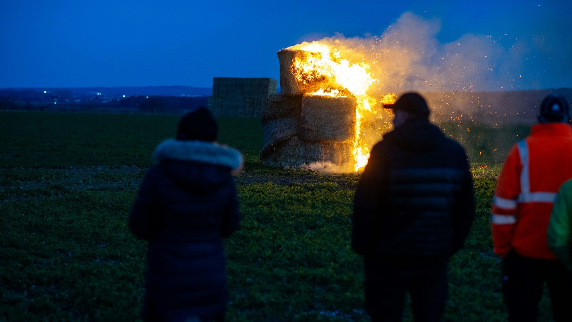 Ein Mahnfeuer aus Strohballen. Im Vordergrund mehrere Personen.