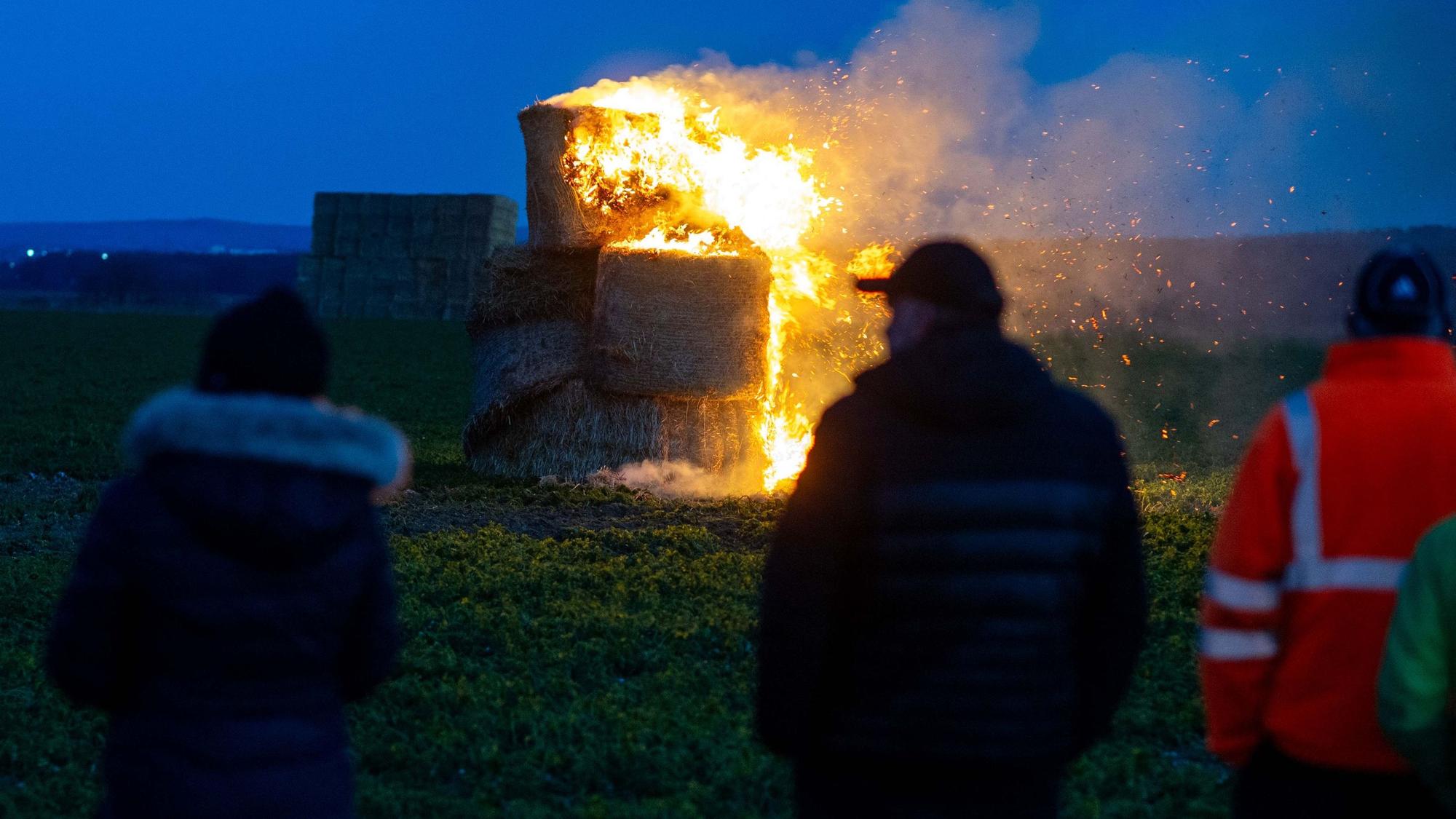 An einem Mahnfeuer der Landwirte an der B266 bei Wißkirchen stehen mehrere Zuschauer.
