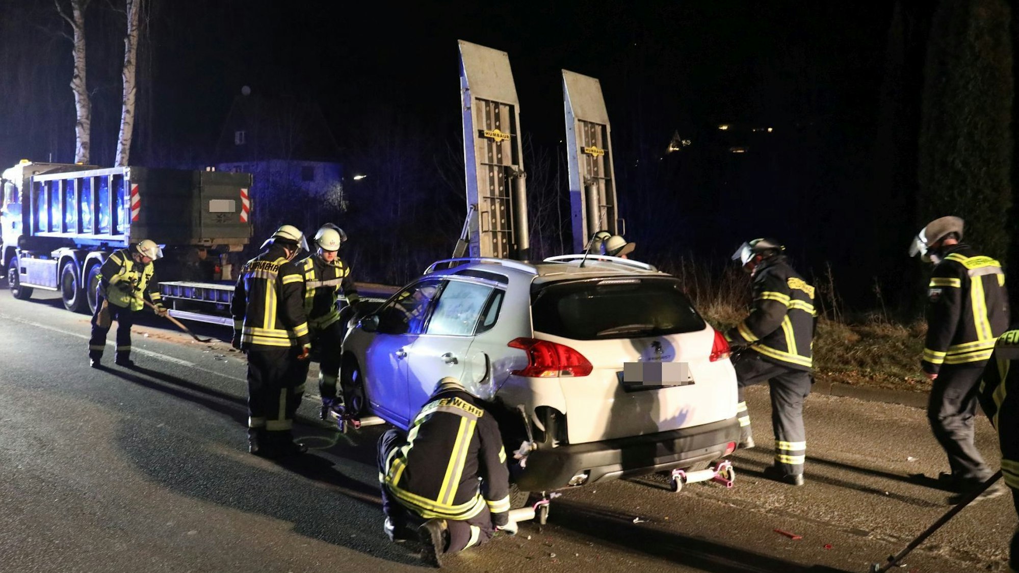 Feuerwehrleute sichern einen weißen Pkw, im Hintergrund steht ein Lastwagen mit Tieflader.