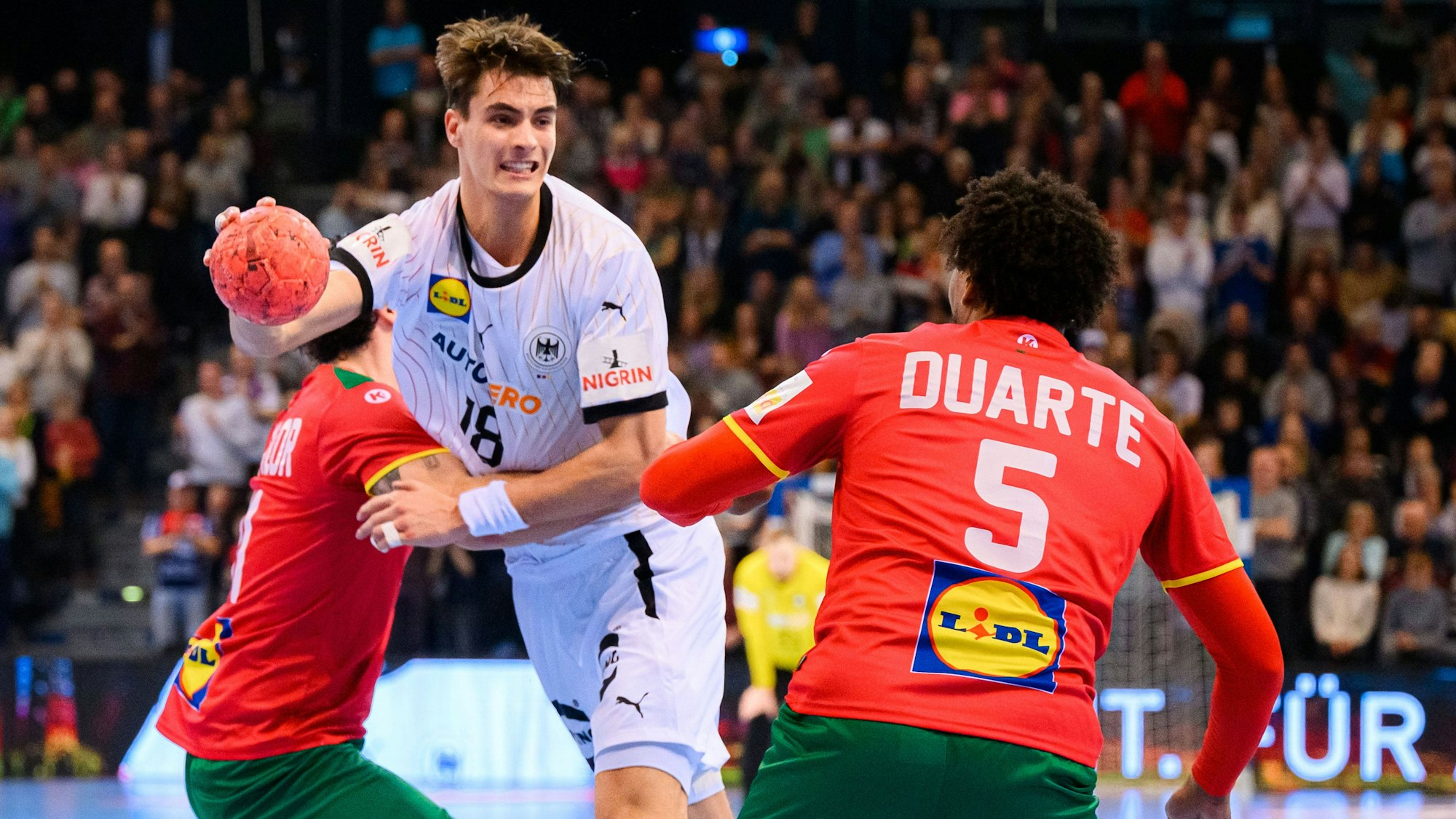 Handballer Julian Köster spielt im deutschen Nationaltrikot. Er setzt sich gegen zwei Gegner aus Portugal durch.