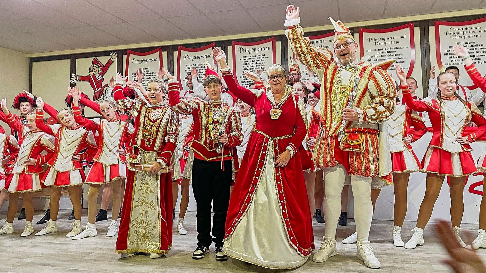 Auf der Bühne stehen die beiden Prinzenpaare, dahinter zahlreiche Gardetänzerinnen und -tänzer, alle in rot-weißen Kostümen.
