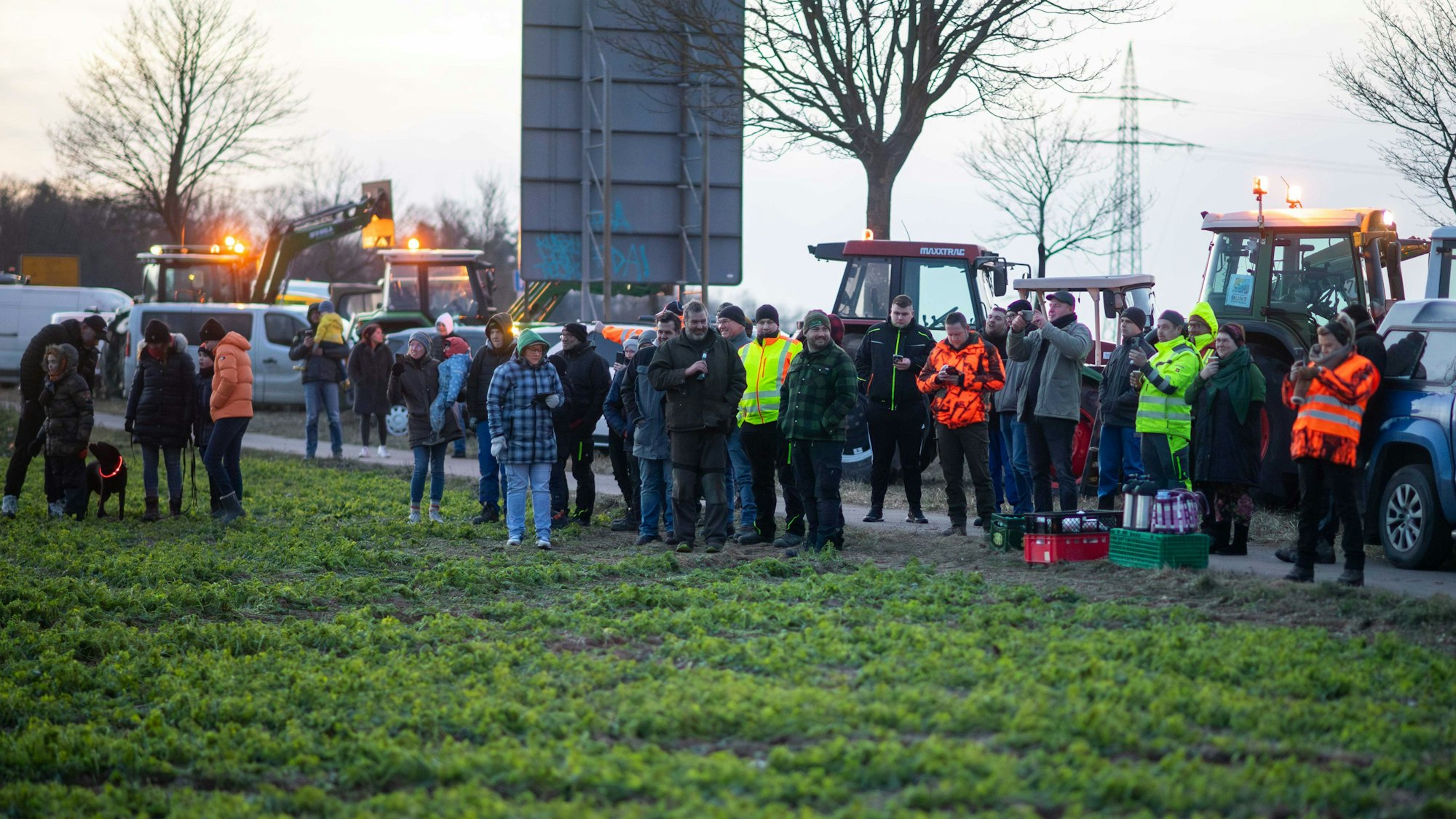 Besucher eines Mahnfeuers an der B266 bei Wißkirchen. Im Hintergrund stehen einige Traktoren.