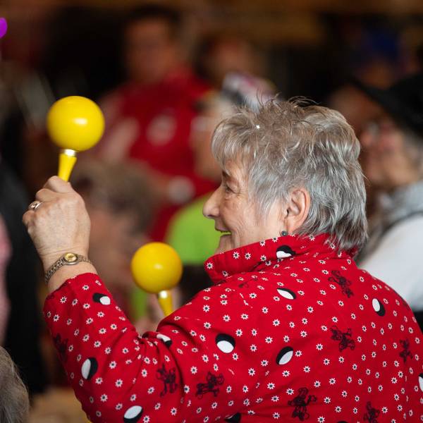 Das Bild zeigt eine Seniorin, die mit zwei Sambarasseln im jecken Rhythmus mitfeiert.