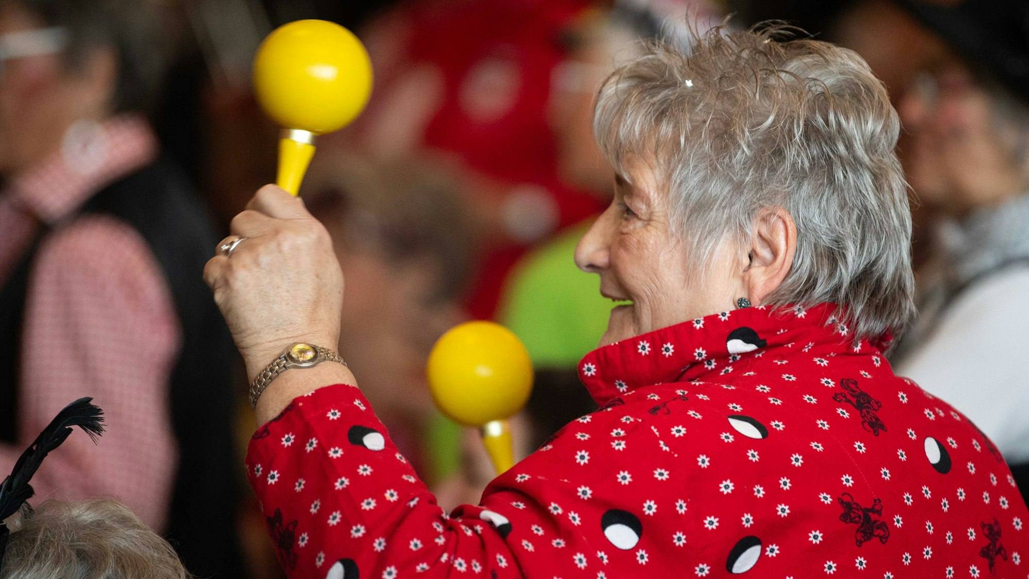 Das Bild zeigt eine Seniorin, die mit zwei Sambarasseln im jecken Rhythmus mitfeiert.