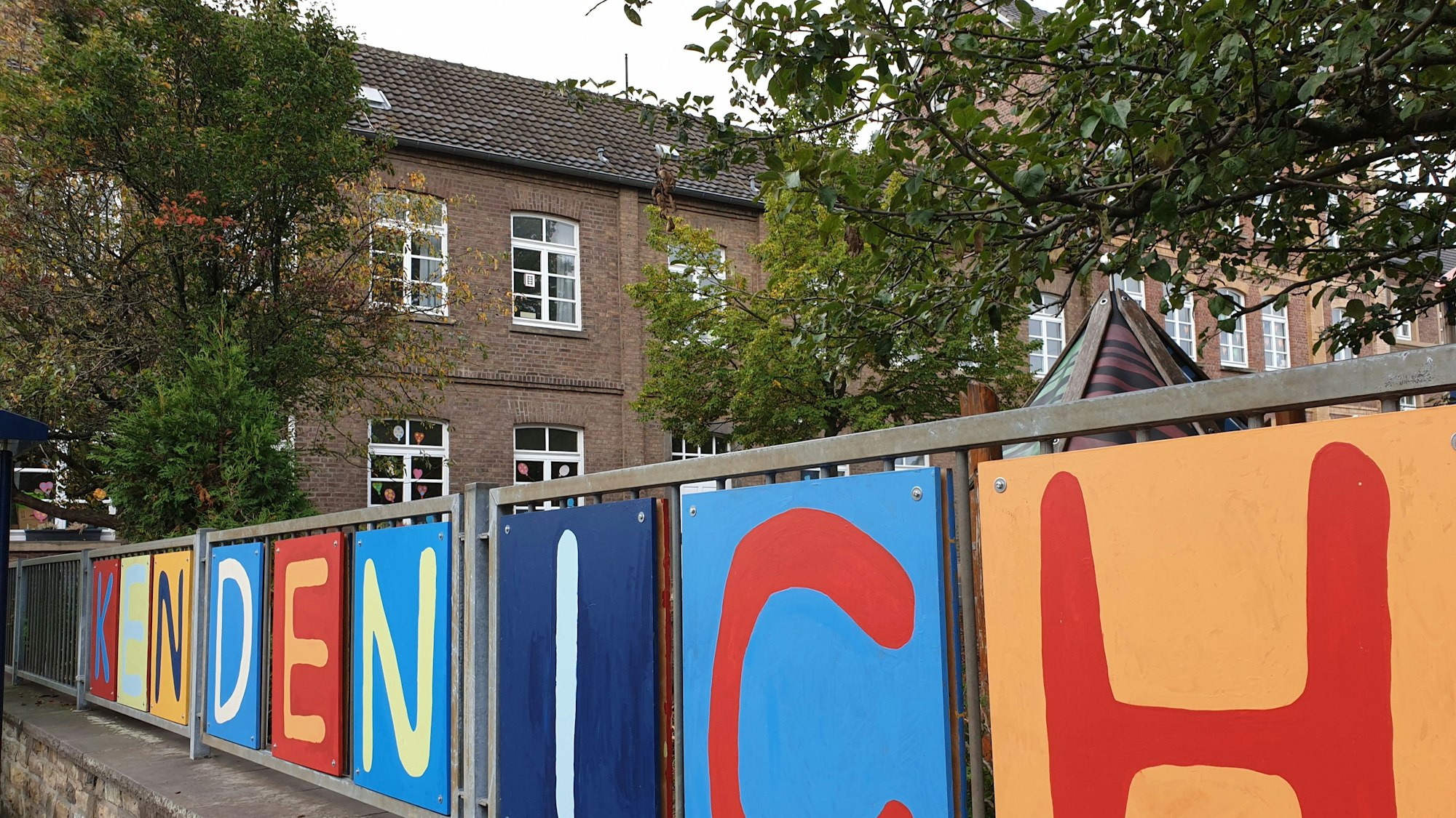 Das Foto zeigt das Wort „Kendenich“ in bunten Lettern am Zaun der Grundschule.