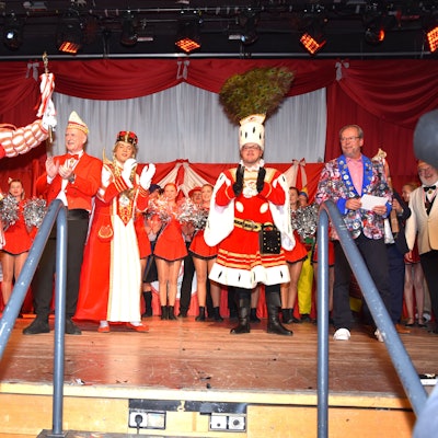 Ein Dreigestirn und eine Tanzgruppe stehen auf einer Bühne.