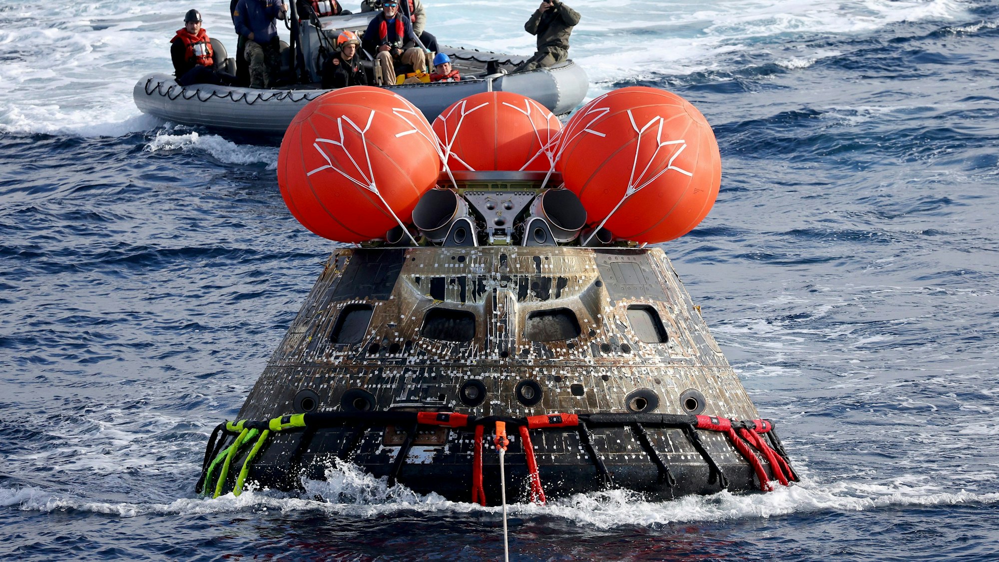 ARCHIV - 11.12.2022, Mexiko, Baja California: Die Kapsel «Orion» der Nasa wird auf das Wellendeck der USS Portland gezogen, nachdem sie nach der erfolgreichen unbemannten Artemis-I-Mondmission im Pazifischen Ozean vor der Küste von Baja California gelandet ist. Die US-Raumfahrtbehörde Nasa hat die zuvor für November 2024 geplante bemannte Mondumrundung «Artemis 2» wegen Problemen mit Rakete und Raumschiff auf September 2025 verschoben. Foto: Mario Tama/Pool Getty Images North America/AP/dpa - ACHTUNG: Nur zur redaktionellen Verwendung und nur mit vollständiger Nennung des vorstehenden Credits +++ dpa-Bildfunk +++