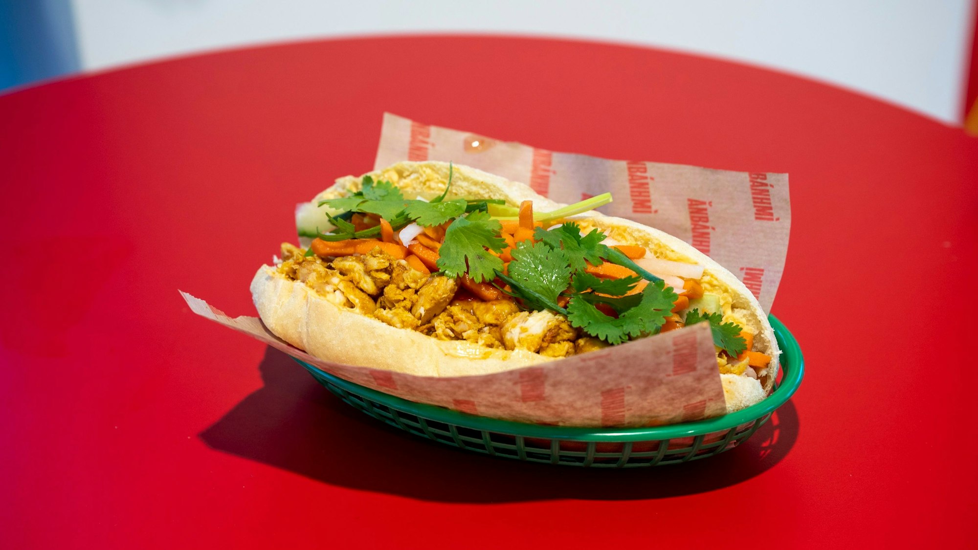 Ein Sandwich liegt in Papier eingepackt auf einem Tisch.