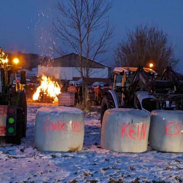 Ein Traktor und Strohballen mit Protest-Aufschriften stehen vor einem Feuer.