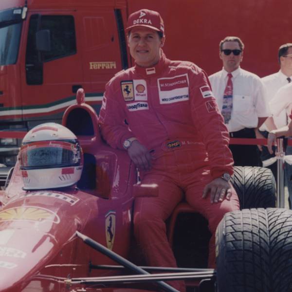 Zu sehen ist Rennfahrer Michael Schumacher, der sich an einen Ferrari lehnt.