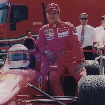 Zu sehen ist Rennfahrer Michael Schumacher, der sich an einen Ferrari lehnt.