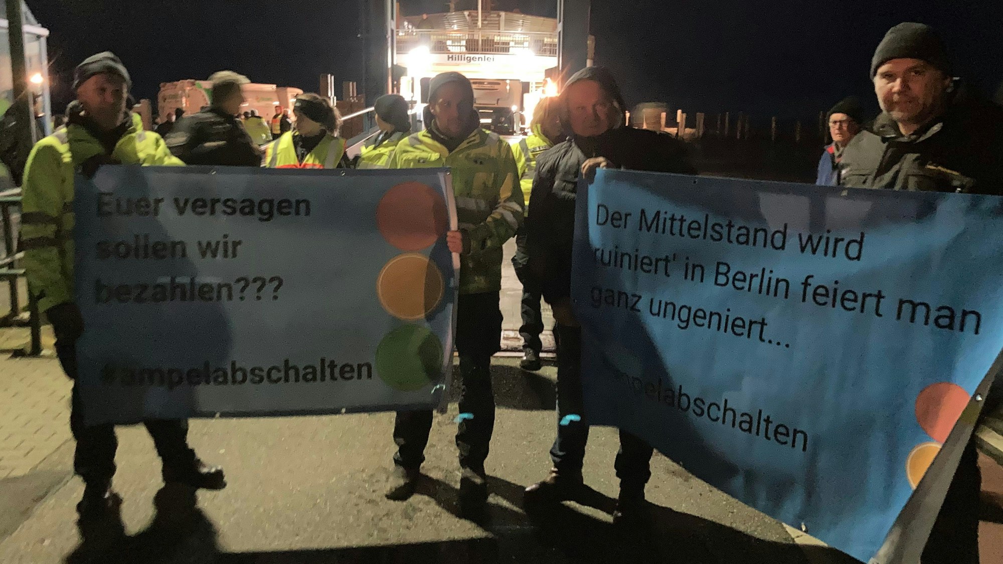 Landwirte stehen mit Plakaten mit der Aufschrift "Euer Versagen sollen wir bezahlen??? #ampelabschalten" am Fähranleger.