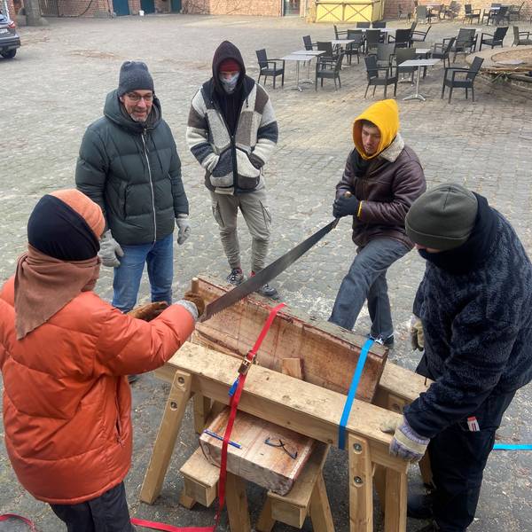 Vor einem Fachwerk-Gebäude sind Holzsäge-Arbeiten im Gange.