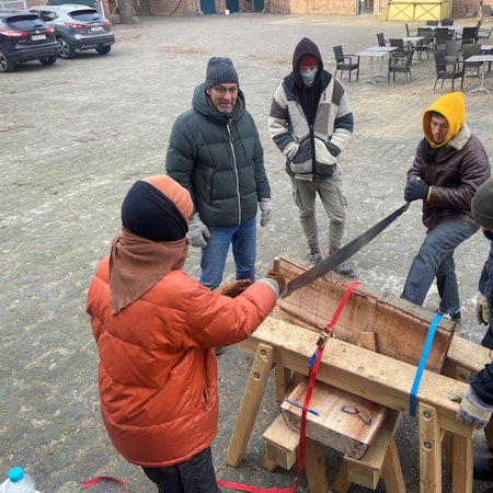 Vor einem Fachwerk-Gebäude sind Holzsäge-Arbeiten im Gange.