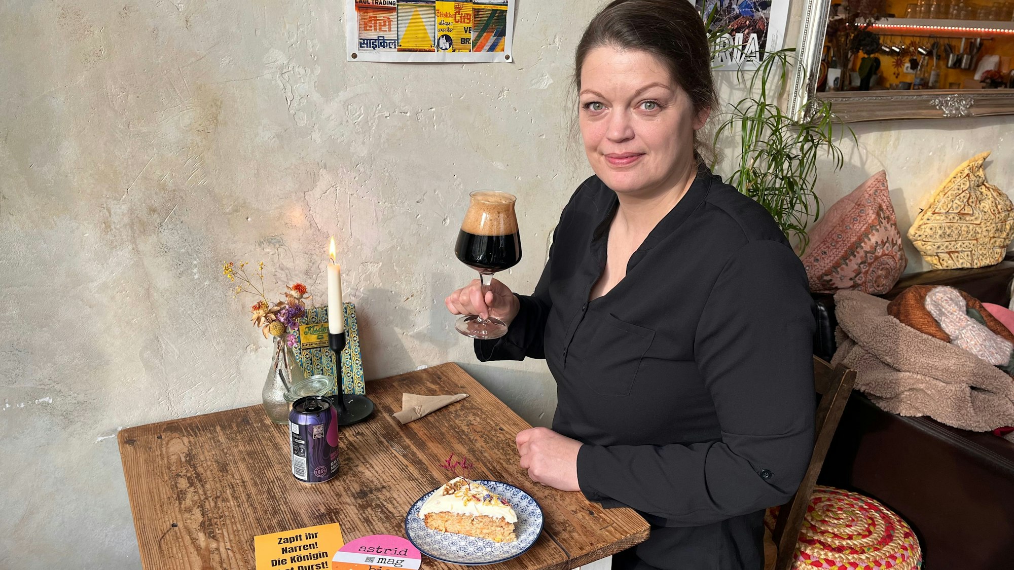 Eine Frau hat sitzt an einem Café-Tisch mit einem Glas Bier in der Hand und einem Stück Kuchen.